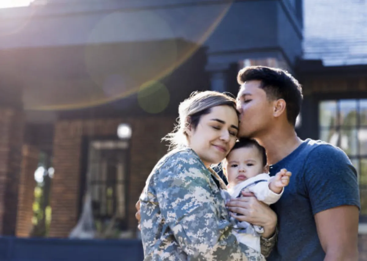 A military couple holding their baby in front of their home